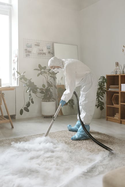 Close-up of a black vacuum cleaner attachment being used to deep clean a patterned area rug with floral motifs in a residential space. The vacuum head is flat against the beige and pastel-colored carpet, and part of the vacuum wand extends upward, held by a person's hand, with the person partially visible in the background wearing casual shoes. The room is well-lit, highlighting the cleanliness of the surface, and the scene reflects professional surface cleaning and maintenance carried out by [COMPANY_NAME], as part of domestic cleaning services in Kingston upon Thames.