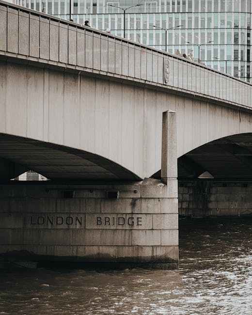 Close-up view of the concrete structure of London Bridge, showing its arches and support pillars spanning over the River Thames. The bridge's surface appears clean and well-maintained, with a smooth, light grey concrete finish. In the background, modern glass buildings reflect light, adding a contemporary urban atmosphere to the scene. The water below is dark with gentle ripples, emphasizing the sturdy construction of the bridge. The image highlights an architectural element of Kingston upon Thames near Kingston Bridge, with natural lighting enhancing the clarity and details of the concrete surfaces. This scene exemplifies surface cleanliness and structural integrity associated with professional maintenance, similar to the detailed surface cleaning and deep cleaning services offered by [COMPANY_NAME] in Kingston upon Thames.